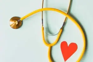 medical stethoscope with red paper heart on white surface